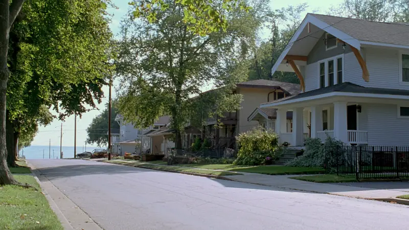 A tree lined street of bungalows with front porches sloping down toward open water