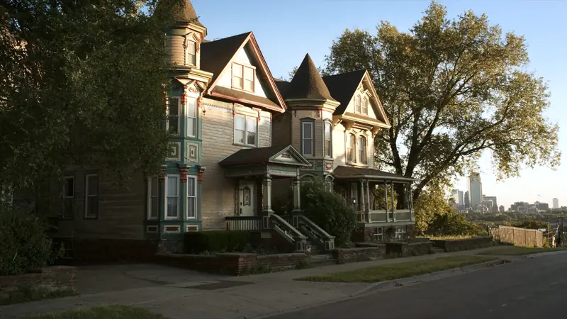 A row of painted Victorian houses with turrets on a hill, a city skyline in the distance at golden hour