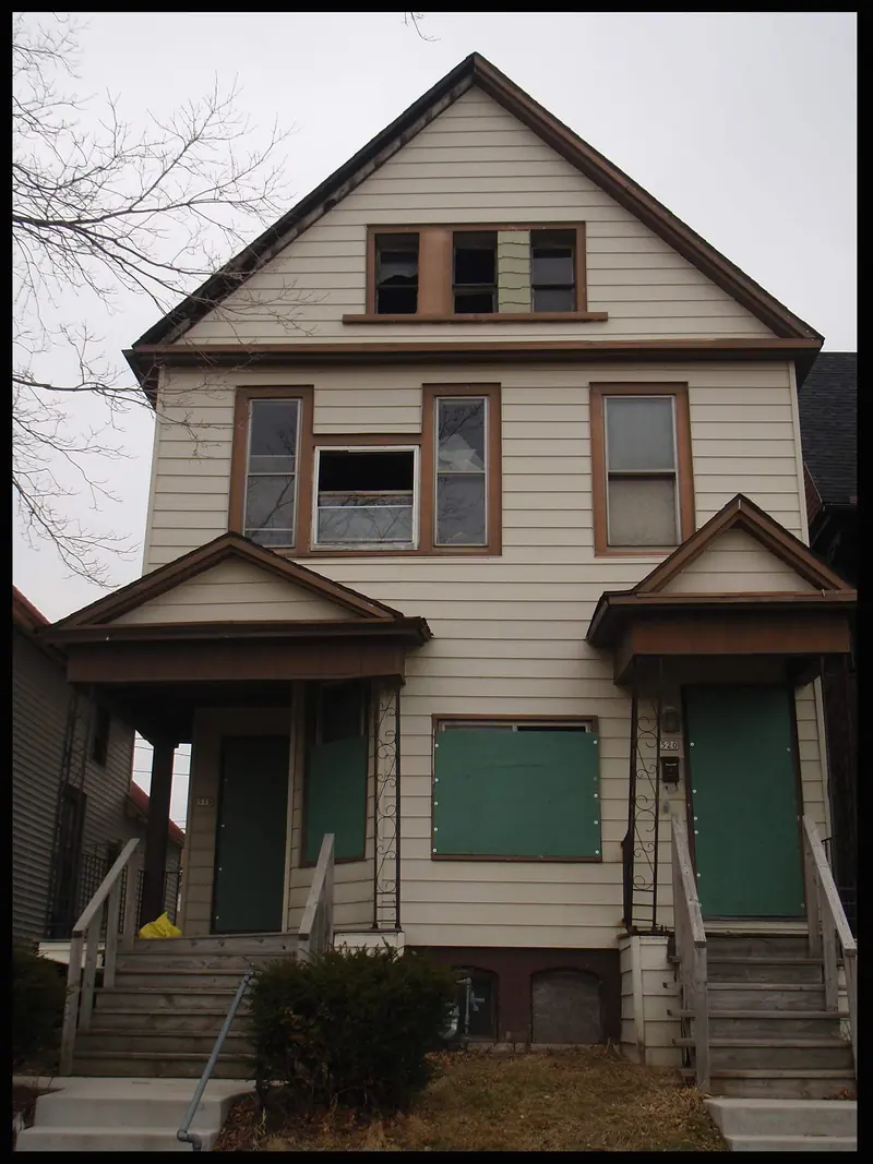 The Glover house before: an old white clapboard house with brown trim, boarded and broken windows