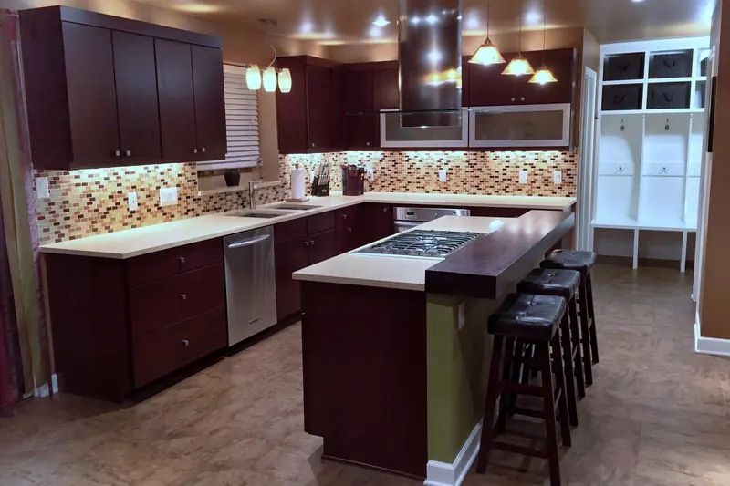 A finished kitchen with dark cabinets, a long island with a raised wood bar and stools, a tile backsplash and pendant lights