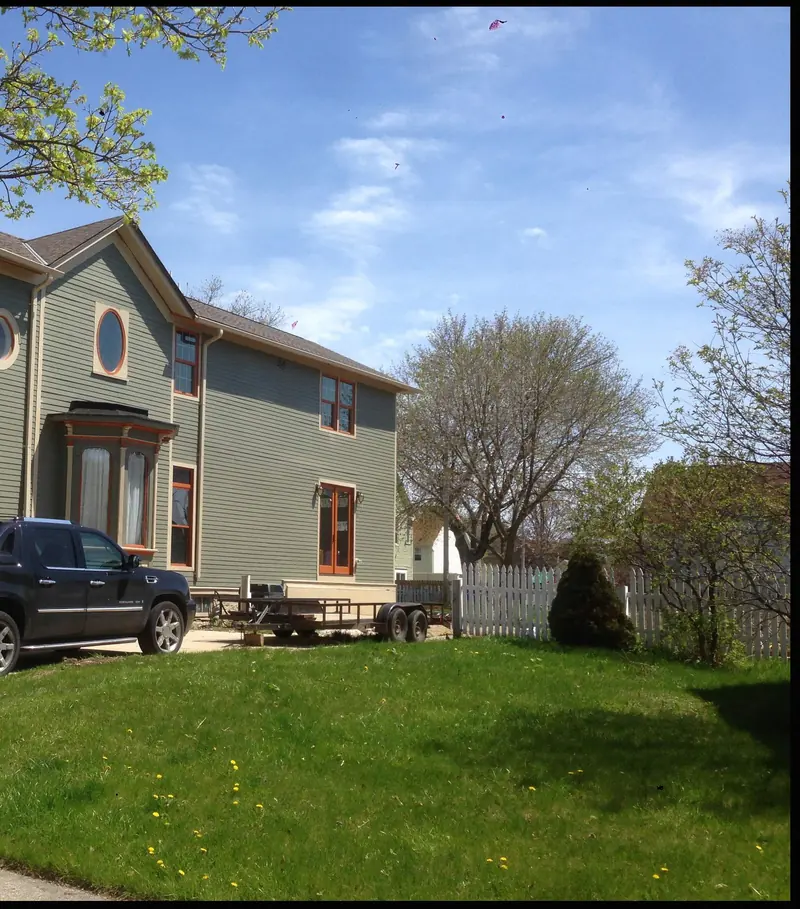The Palmer house after: the same house repainted sage green with white trim, a lawn and a picket fence
